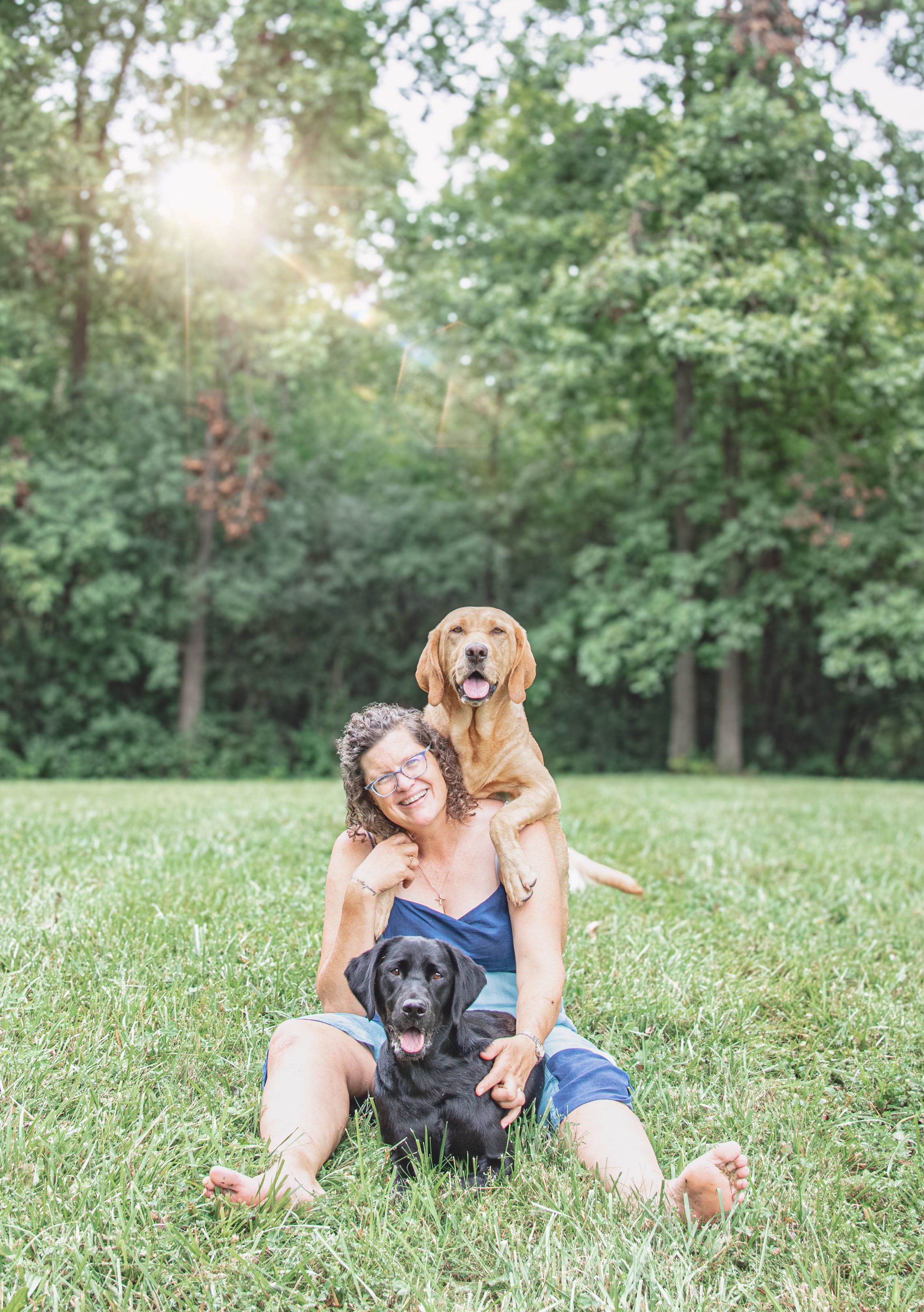 Woman sitting in a field with two dogs