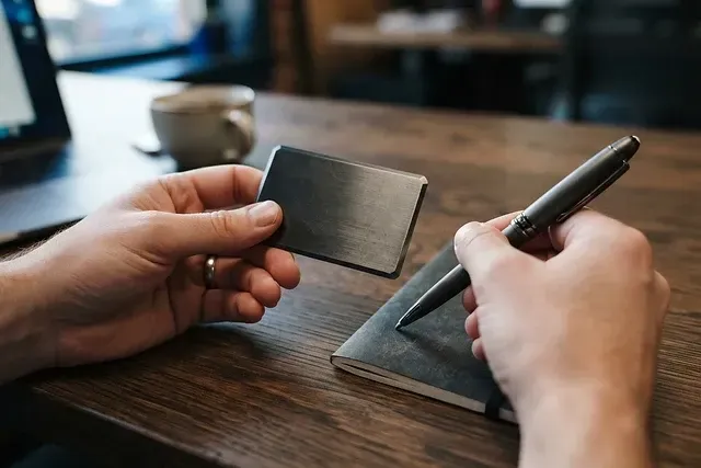 Close-up of hands holding a metal credit card on a dark wood desk