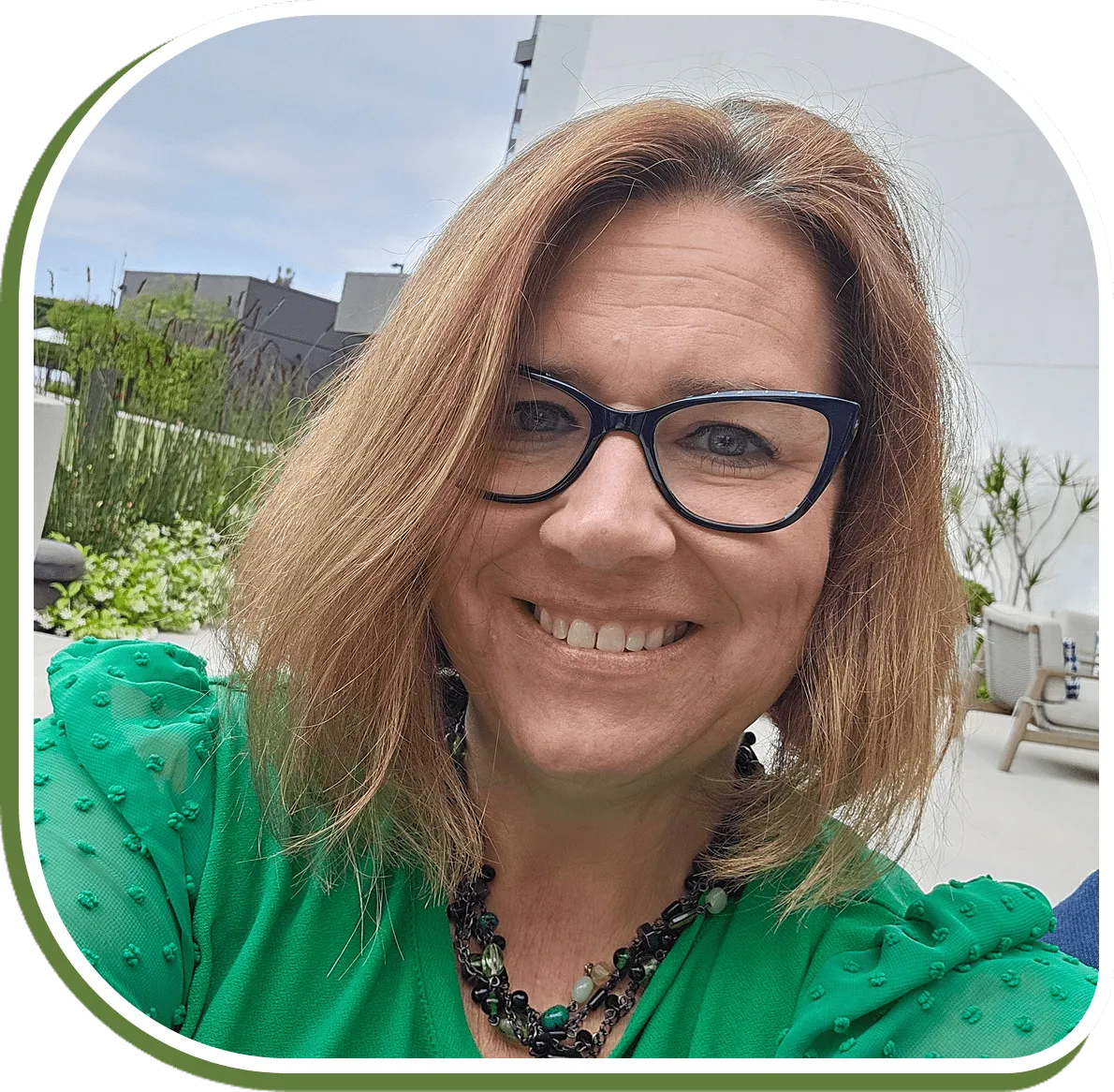 Smiling woman with glasses outdoors in a green top.