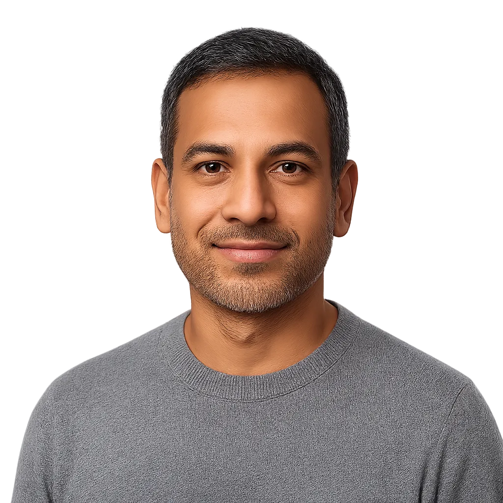 Confident middle-aged South Asian man smiling, head-and-shoulders portrait on light background.