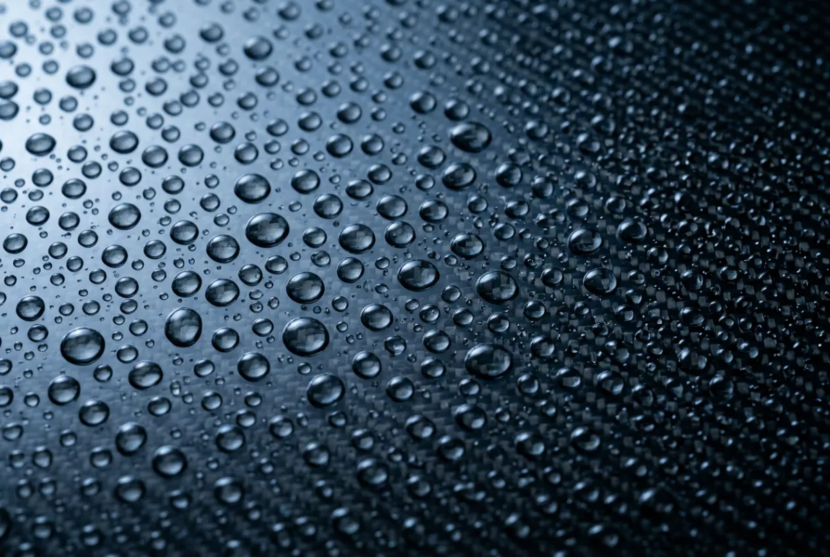 Macro high-contrast shot of intense water beading on a ceramic-coated carbon fiber hood