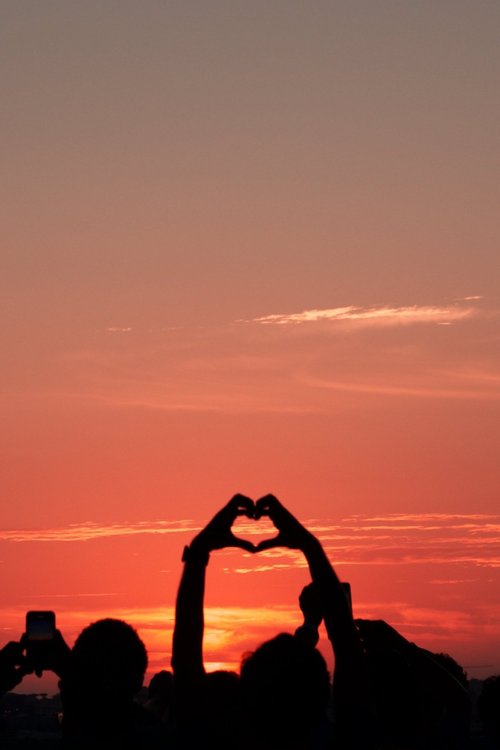 People silhouette at sunset with one person forming a heart shape with their hands.
