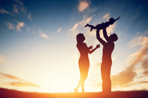 Parent holding child silhouette at sunset