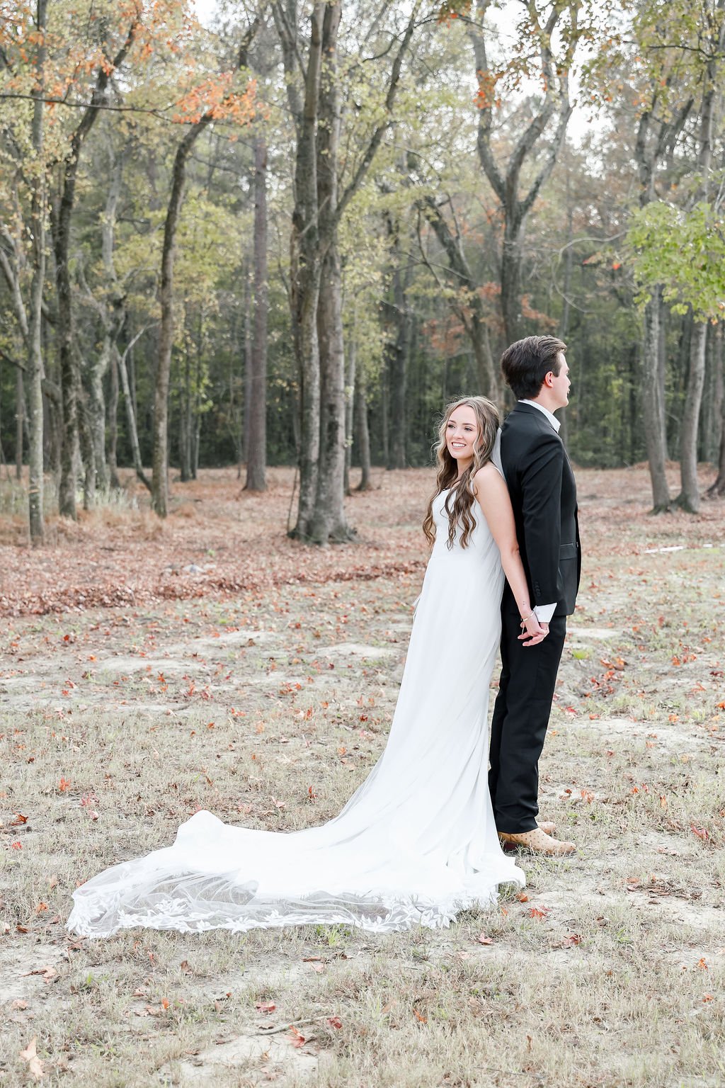 A bride and groom stand back-to-back in an outdoor wooded setting