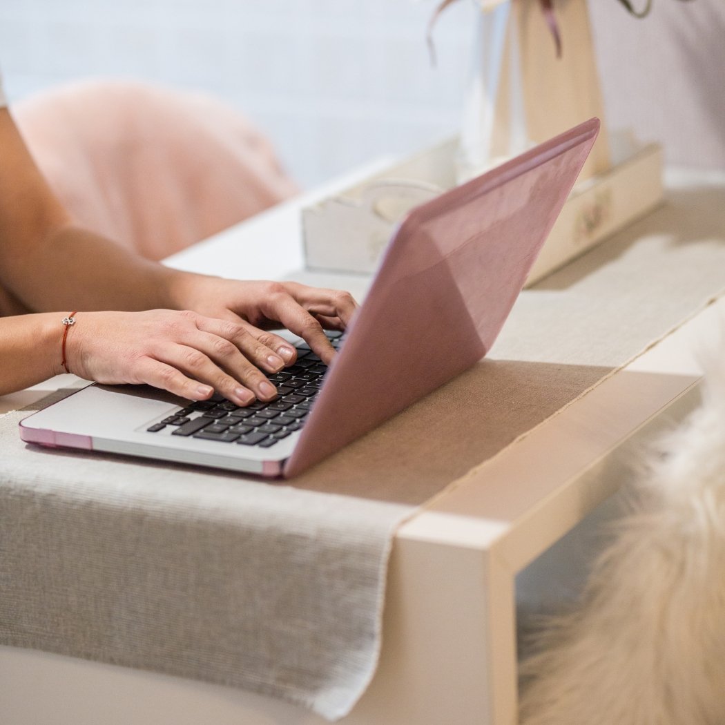 Person tippt auf einem rosa Laptop
