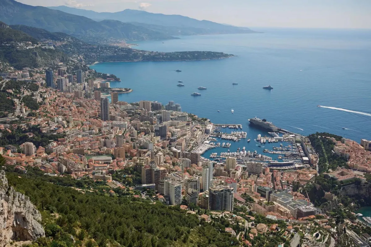 Wide-angle shot of Monaco and the Riviera coastline, overlooking the harbor, cruise ship, and surrounding mountains.