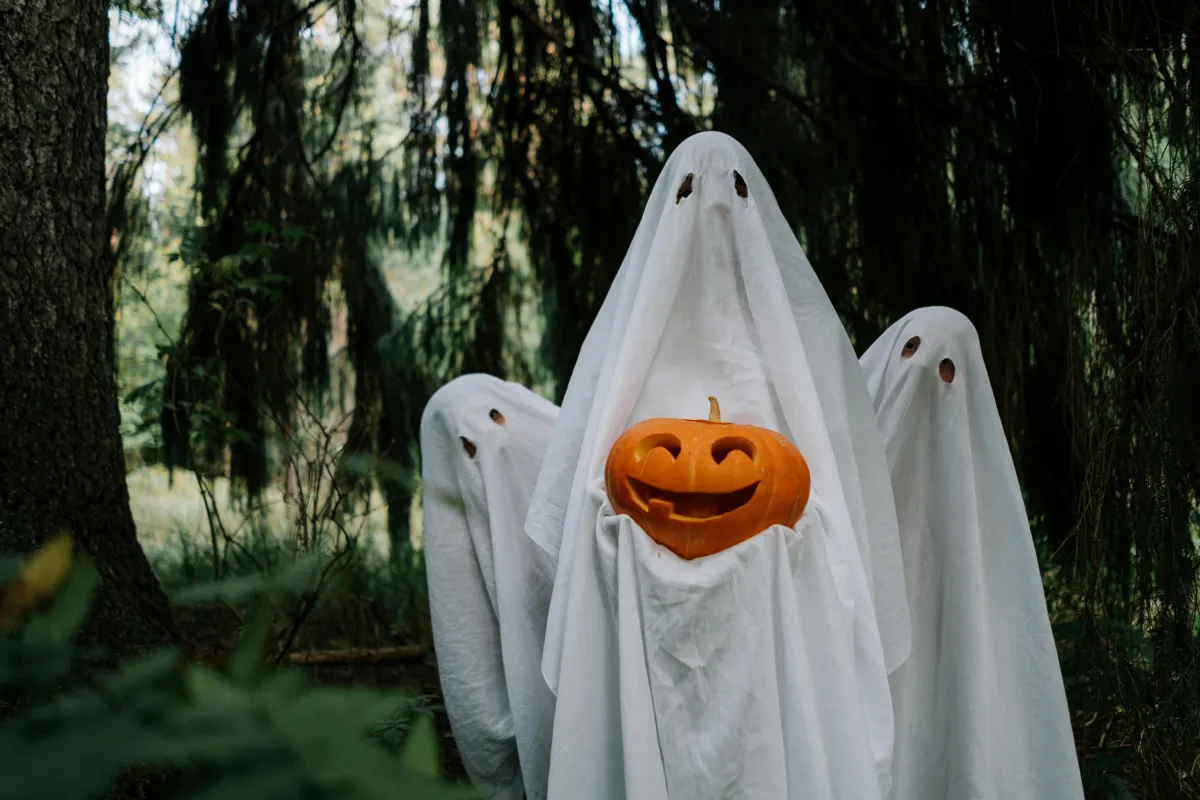 Three ghosts holding a pumpkin, surrounded by trees