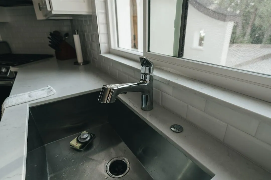 Stainless steel kitchen sink and chrome faucet under a window