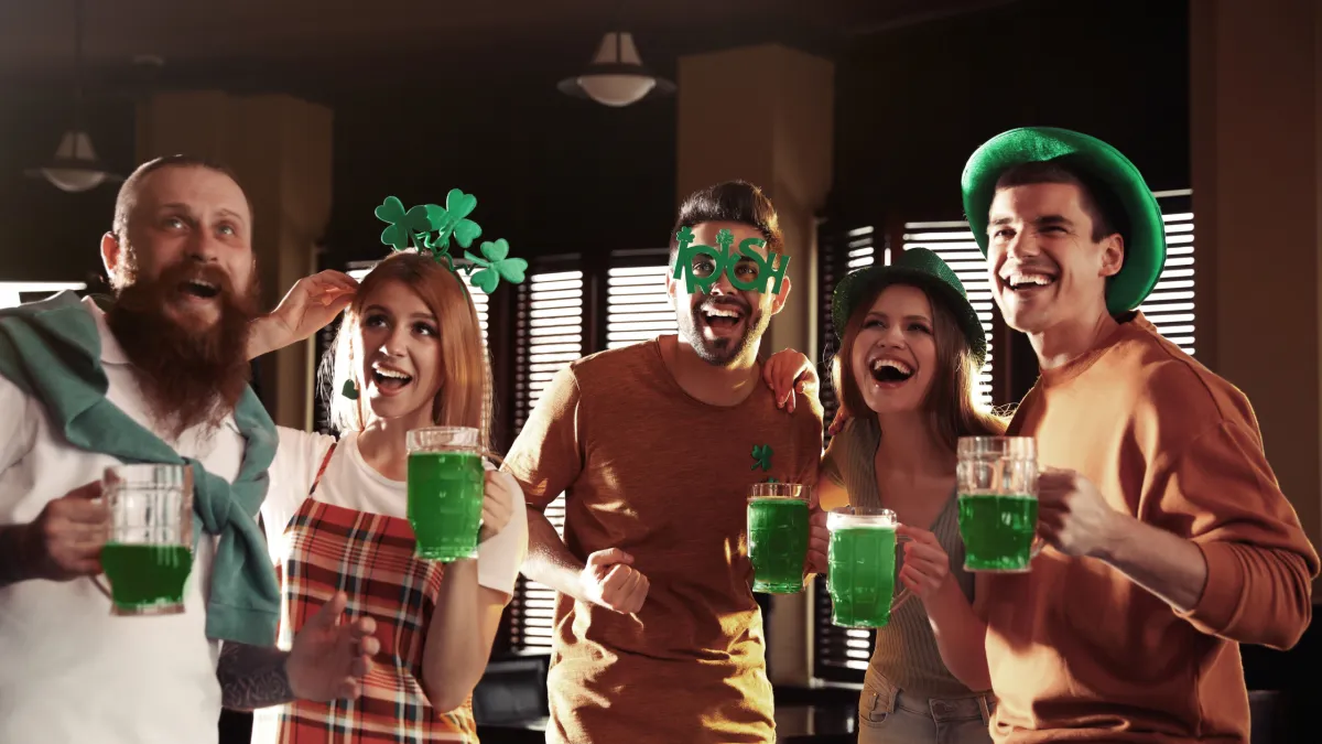 A crowded bar filled with people wearing green and raising pints of beer in celebration of Saint Patrick's Day.