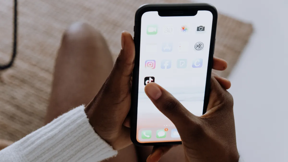 A person holding a smartphone using their right hand. The phone's screen displays various app icons including social media apps like Instagram and Facebook.