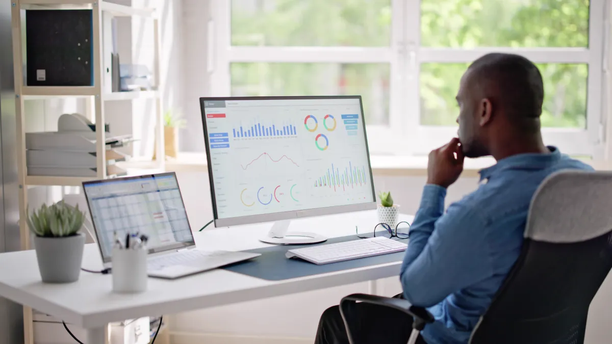 A business owner managing personal finance, sitting at a desk with a computer and monitor, deep in concentration.