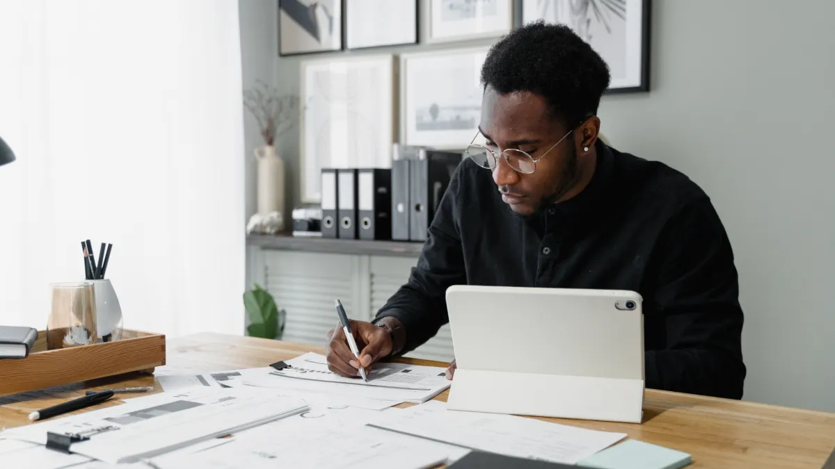 A small business owner carefully reviewing accounting documents at a well-organized desk, using a tablet and taking notes