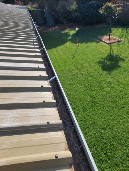Clean, debris-free gutter on a metal roof overlooking a well-maintained green lawn, illustrating the results of professional gutter cleaning for optimal drainage.