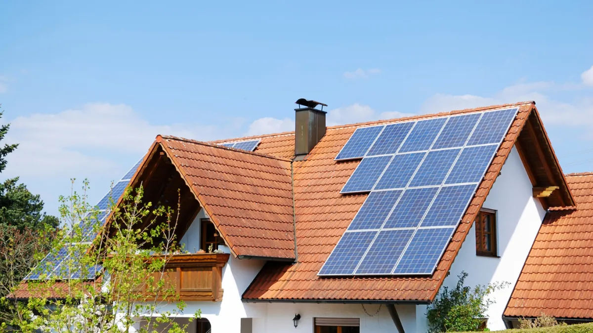 Solar panels installed on a red-tiled roof under a clear blue sky, highlighting the importance of regular cleaning and inspections to detect damage and maintain energy efficiency.