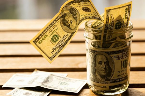 Modest salary cash stuffed in a jar on a wooden-slatted table