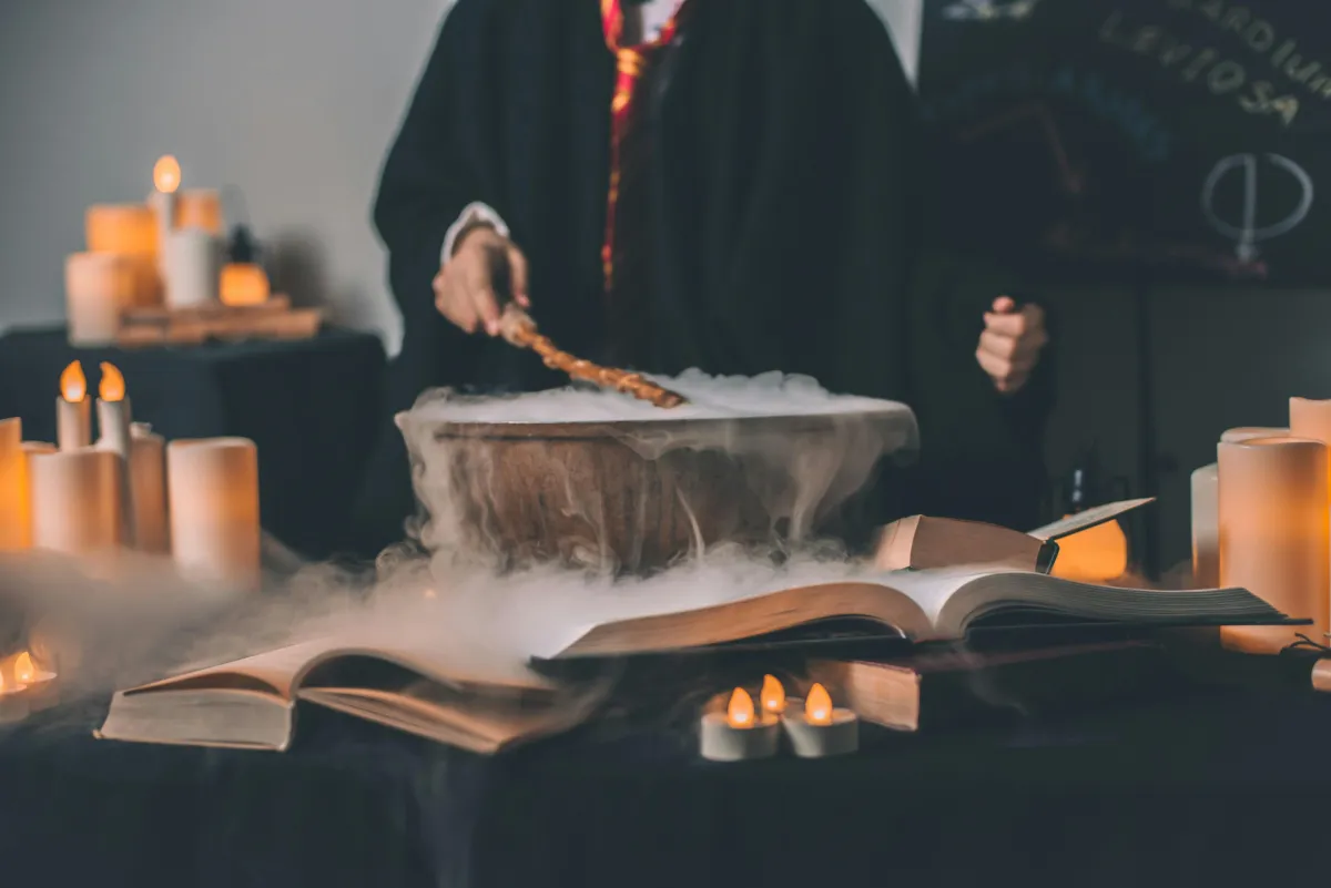 Person holding magic wand, steaming bowl on table with many lit candles