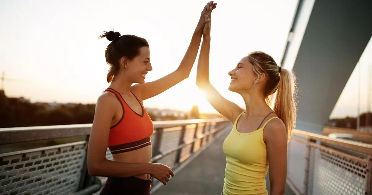 Two fit women high-fiving on a running track, celebrating progress in regaining core strength and stability through targeted exercises.