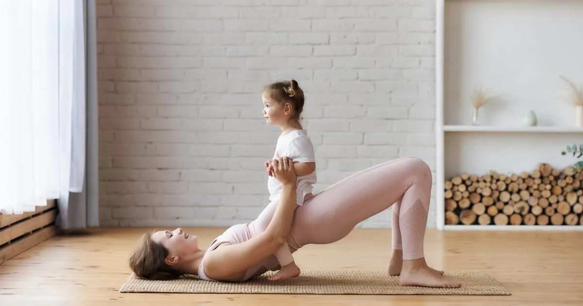 Fit woman performing a bridge exercise with a small baby on her hips, focusing on strengthening the pelvic floor and healing diastasis recti through targeted movements.