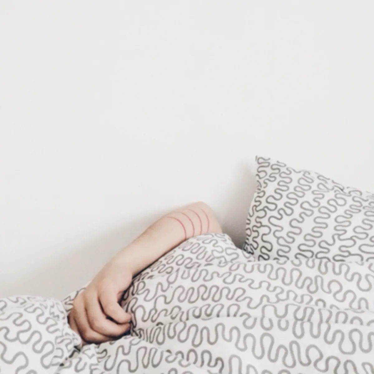 Caucasian arm and hand sticking out from under a beige coloured duvet