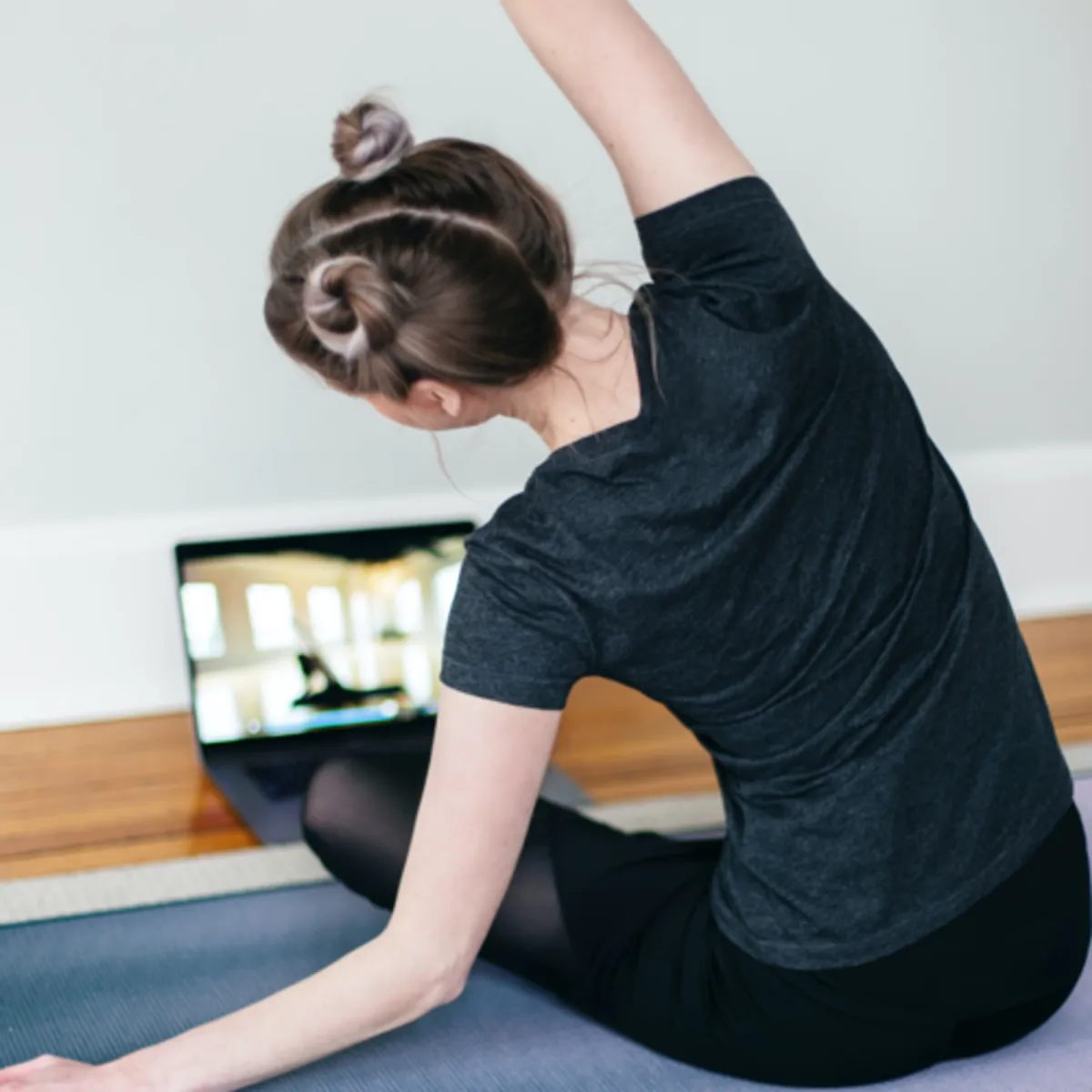 Caucasian woman in a black tshirt leaning to the left practicing yoga with a computer