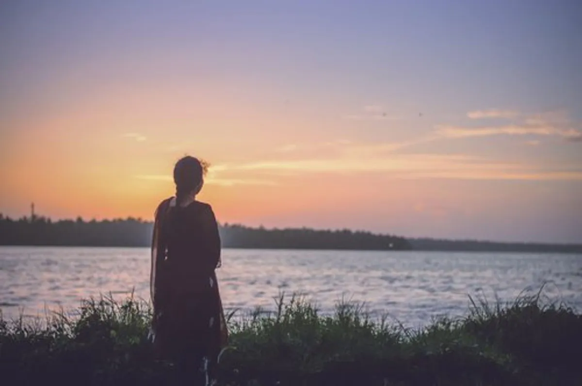 Silhouette of a woman overlooking a calm lake at sunset