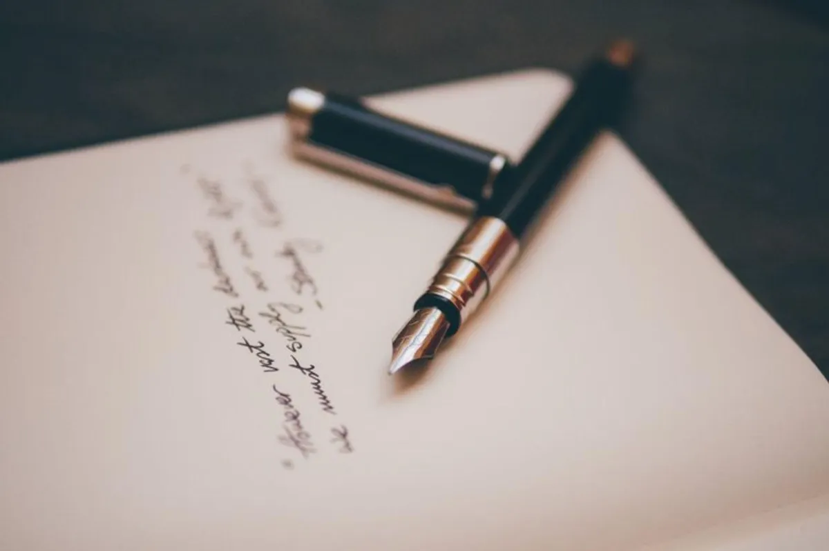 Cream coloured paper with a black and gold ink pen and it's lid resting next to some black handwritten script