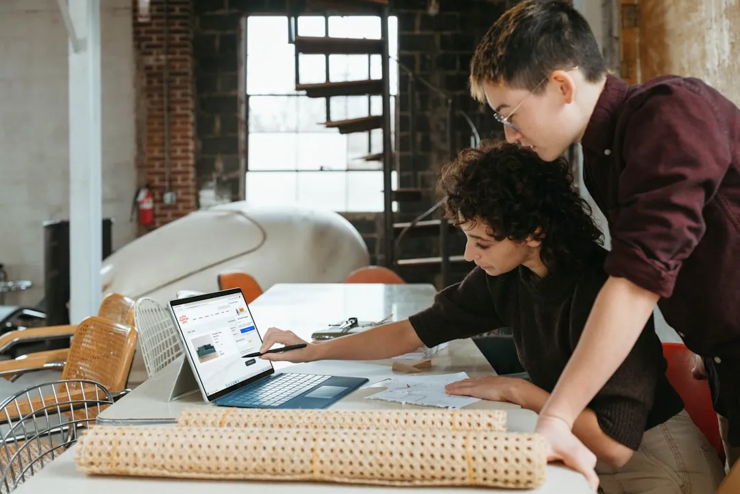 Two young entrepreneurs collaborating on a laptop in an industrial-style workspace, discussing designs and strategies for integrating AI chatbots into their small business operations.