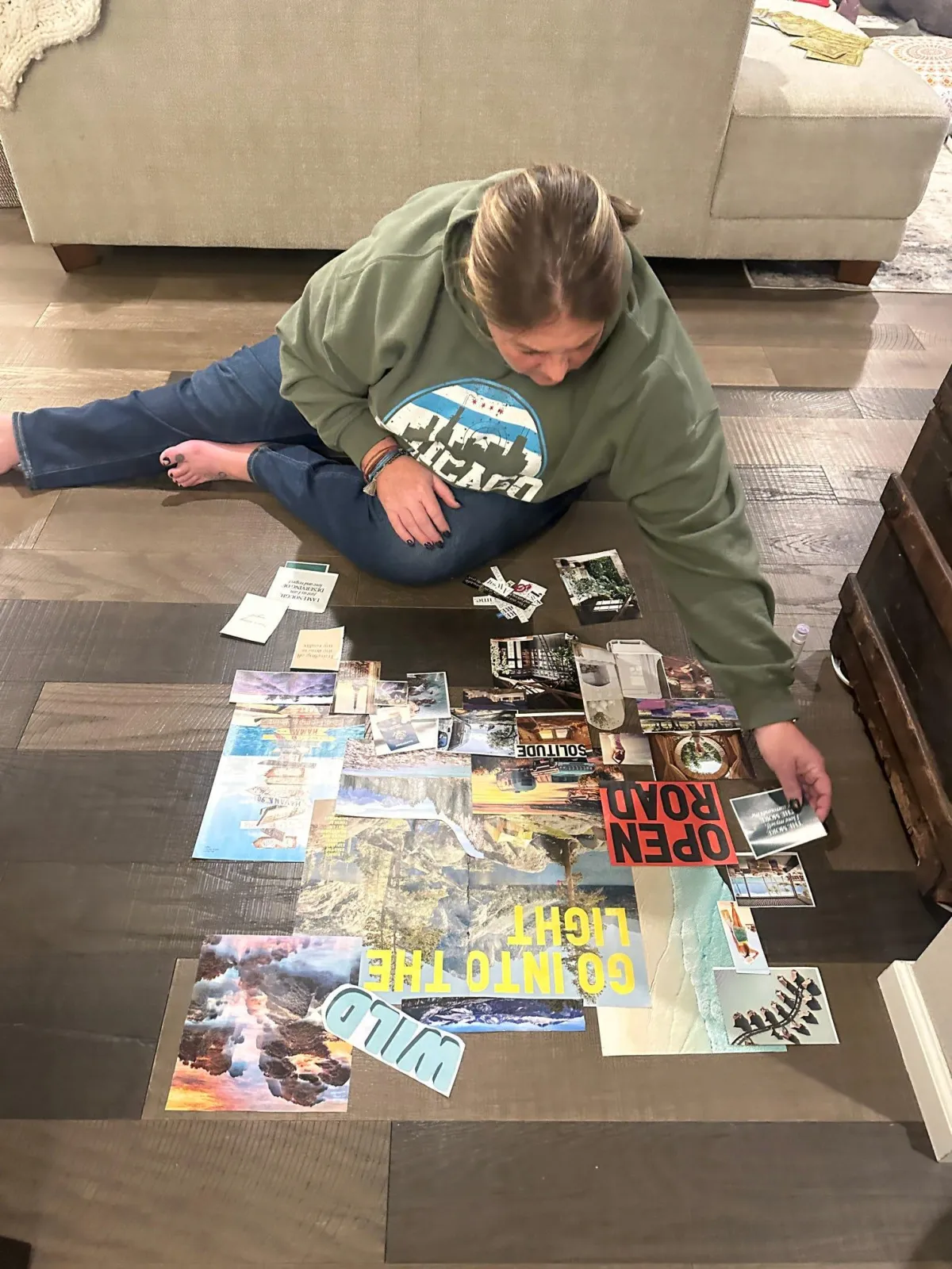 Person sitting on the floor assembling a collage or vision board with various photos, magazine cutouts, and text pieces spread out around them.