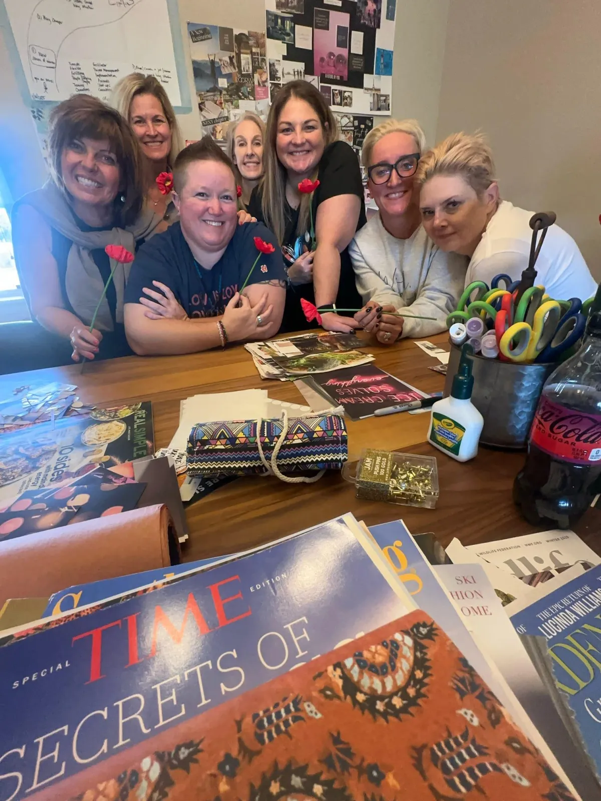 Group of women gathered around a craft table covered with scrapbook materials, smiling at the camera during a creative session.