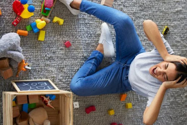 Mum yelling with hands on head sitting amongst toys