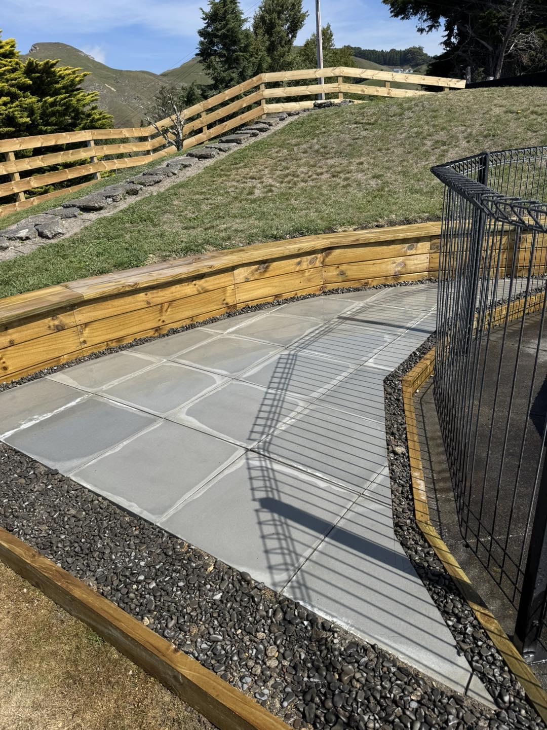 Timber retaining wall and grey paved walkway on sloped section, showing retaining wall and landscaping services in Hastings, Hawke's Bay by Mitch's Maintenance
