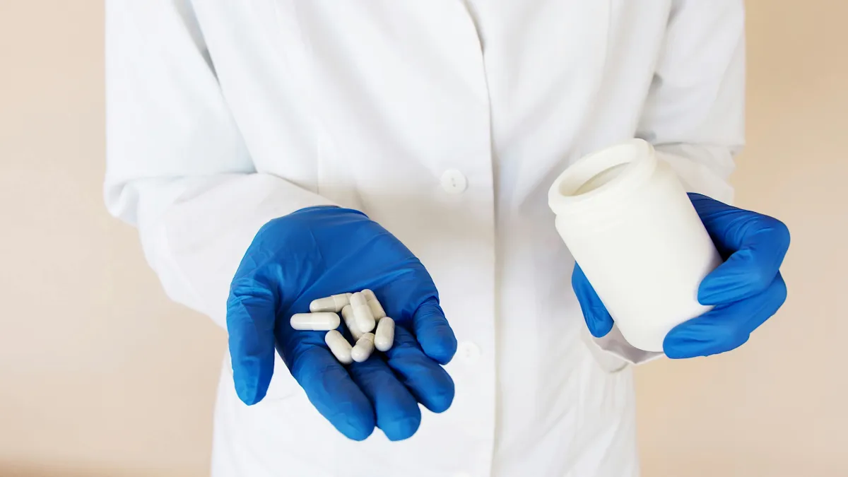 white lab coat and blue gloves holding pills