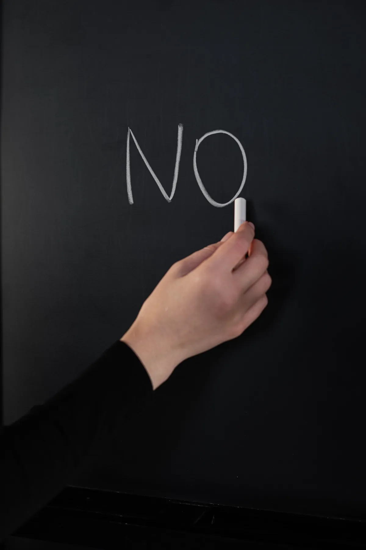 hand with chalk writing the word no on chalkboard