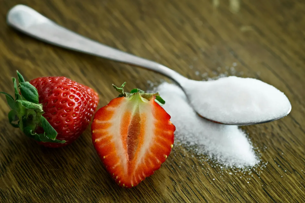 strawberries on brown table with spoon of white sugar