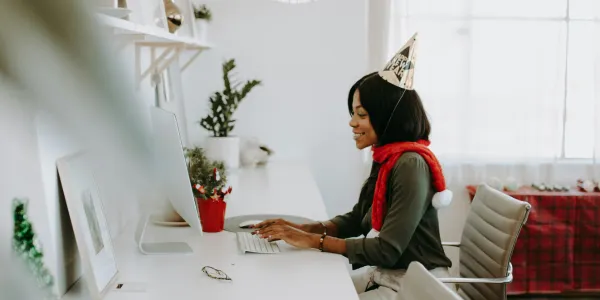 Woman in a party hat typing at a laptop in a white aesthetic office.