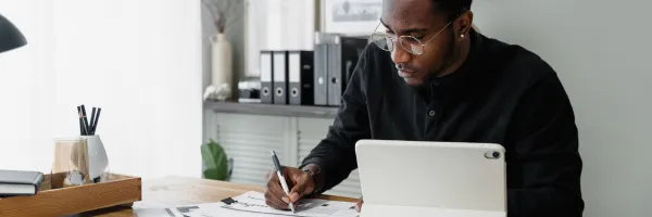 Man in dark shirt sitting at a laptop making notes preparing for meeting with an accountant for his small business
