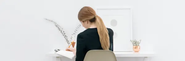 Back of a woman sitting at a desk with a natural aesthetic writing in a notepad