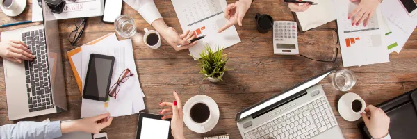 Close up of table of business meeting, showing hands and paperwork.