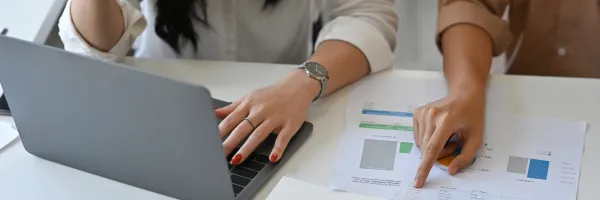 Close of of women's hands with a laptop and paperwork.
