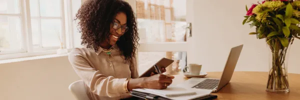 Smartly dressed woman smiling working on her laptop and taking notes