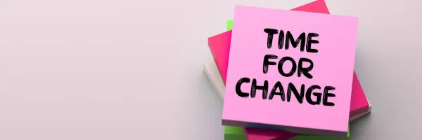 A stack of pink sticky notes with the top pad being pink with Time For Change written on it.
