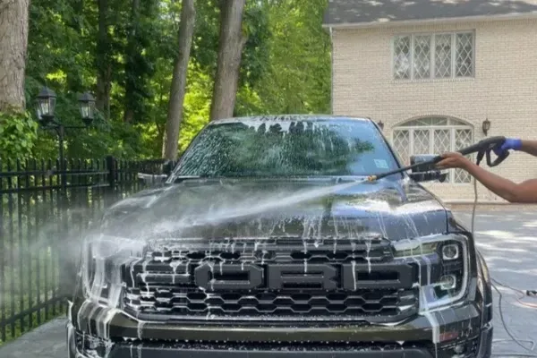 Ford truck covered in soap being pressure-washed in driveway for exterior detailing