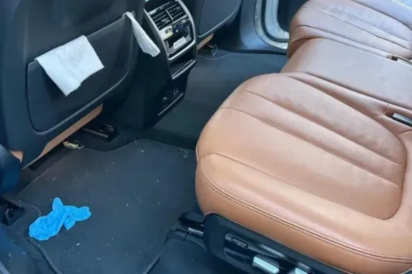 Dirty rear car floor with debris and brown leather seats before interior detailing.