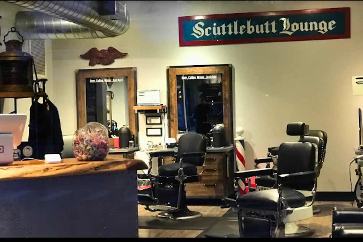 Interior of Scuttlebutt Barbershop in Portsmouth, NH featuring vintage barber chairs, wood-framed mirrors, and a wall sign that reads 'Scuttlebutt Lounge'.