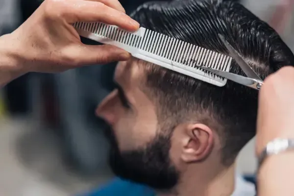 Barber cutting a man’s hair with scissors and comb at Scuttlebutt Barbershop in Portsmouth, NH