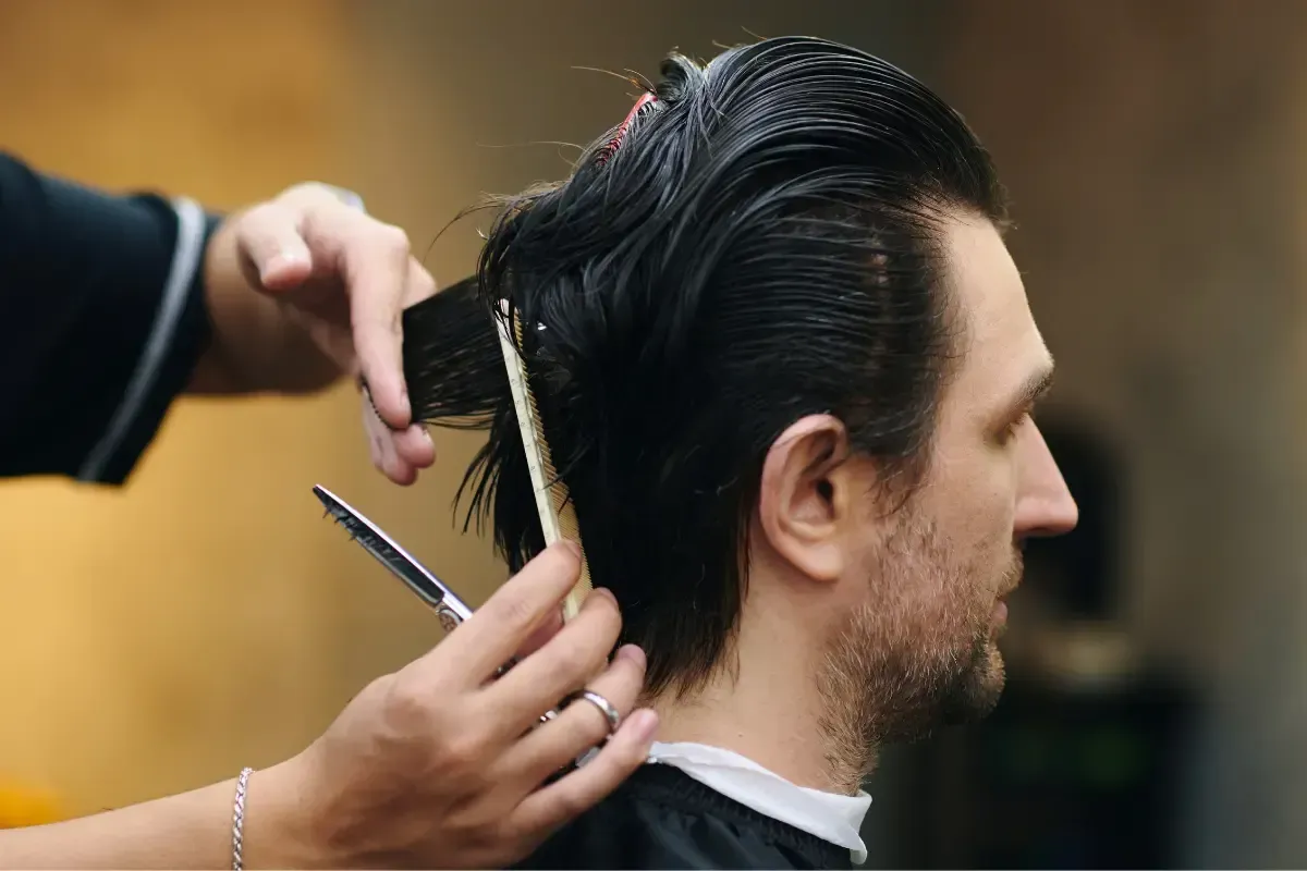 Barber cutting a man’s medium-length dark hair with scissors and comb at Scuttlebutt Barbershop in Portsmouth NH