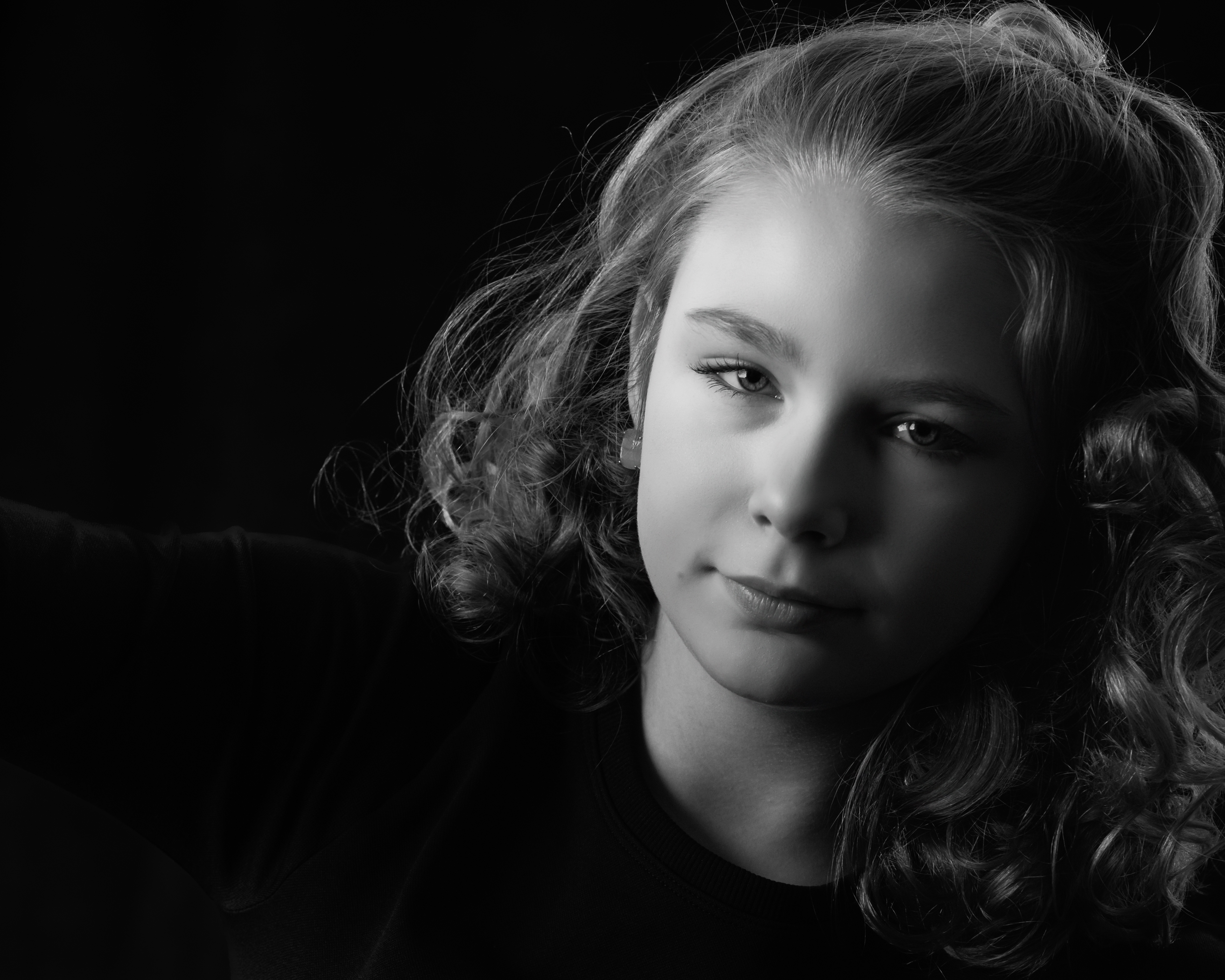 A close-up black-and-white portrait of a young girl with softly curled hair, her face gently turned toward the light as she looks calmly toward the camera (Evidence), conveying a feeling of thoughtfulness, calm, and inner steadiness (Emotion), reflecting the quiet confidence and sense of self that emerges as she grows into who she is becoming (Elevation).