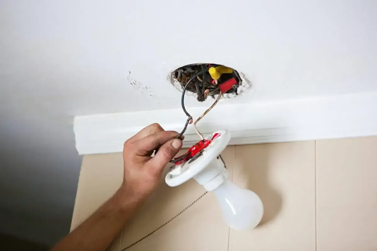 A man fixes a ceiling light bulb, carefully balancing on a ladder to reach it.