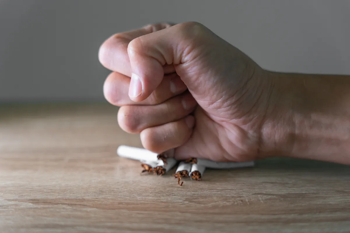 Mano cerrada en puño aplastando cigarrillos sobre una mesa, simbolizando la decisión de dejar de fumar y vencer la adicción al tabaco.