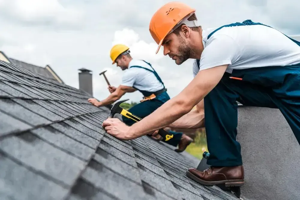 Two professional roofers in safety gear performing roof repairs on a sloped residential roof under daylight, emphasizing the importance of hiring expert contractors in Bellevue.
